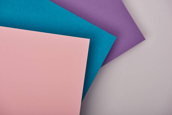 top view of blue, purple and pink paper sheets with copy space on white background