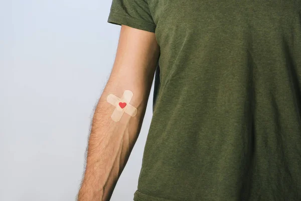 グリーンの シャツで患者の部分的なビューが血寄付の概念 灰色の背景に絆創膏します — ストック写真