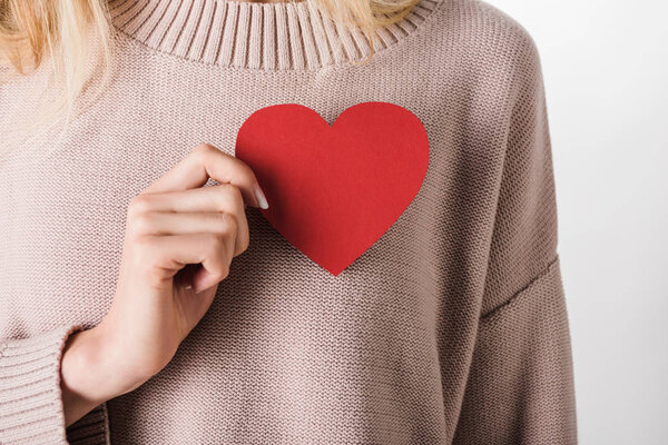 Cropped view of blonde woman in beige sweater holding paper heart on white background