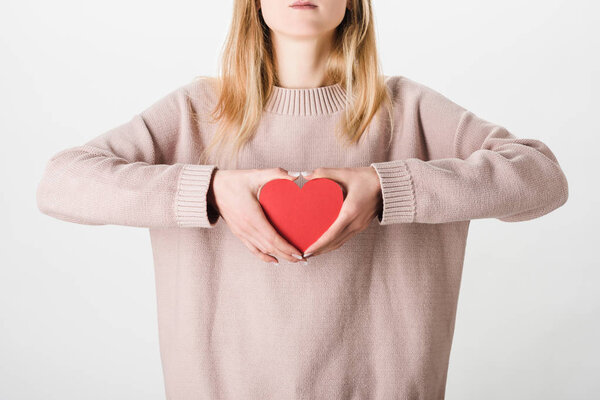 Частичный вид женщины в бежевом свитере с бумажным сердцем на белом фоне

