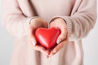 Partial view of woman in beige sweater holding toy heart  clipart
