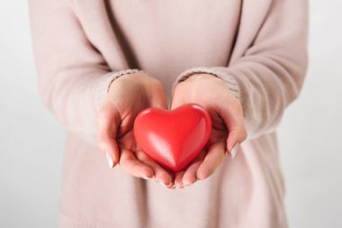 Cropped view of woman in beige sweater holding toy heart  clipart