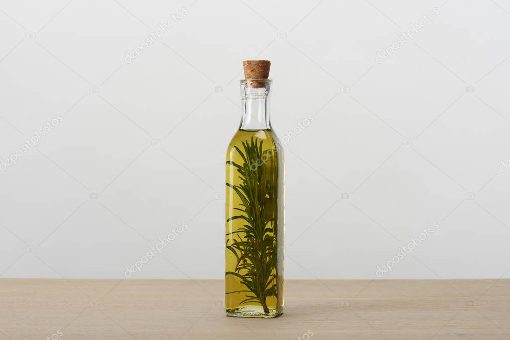 corked bottle of flavored oil with rosemary branch inside on grey surface