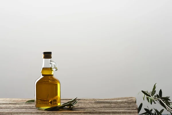 bottle of oil and olive tree leaves isolated on grey