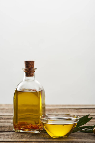bottle and glass bowl of olive oil, olive tree leaves and olives on wooden surface