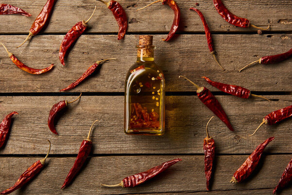 top view of bottle with flavored oil and red hot chili peppers on wooden background