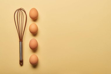 top view of balloon whisk and eggs  on yellow background clipart