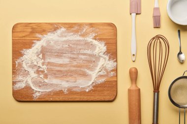 top view of wooden chopping board with flour and cooking utensils on yellow background  clipart