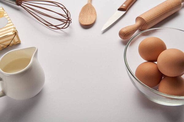 close up of cooking utensils, butter, jar with milk and eggs in bowl on grey surface