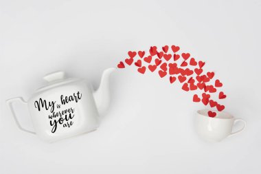 top view of tea pot, cup and heap of red paper cut hearts on white background with 