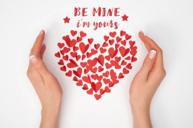 cropped view of female hands near heart shaped arrangement of small red paper cut hearts with 