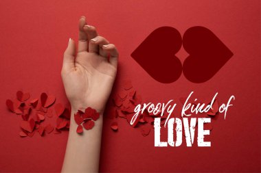 cropped view of female hand with paper cut decorative hearts on red background with 