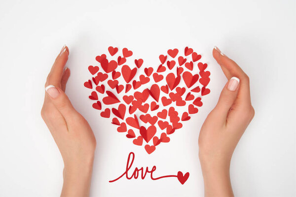 cropped view of female hands near heart shaped arrangement of small red paper cut hearts with "love" lettering 