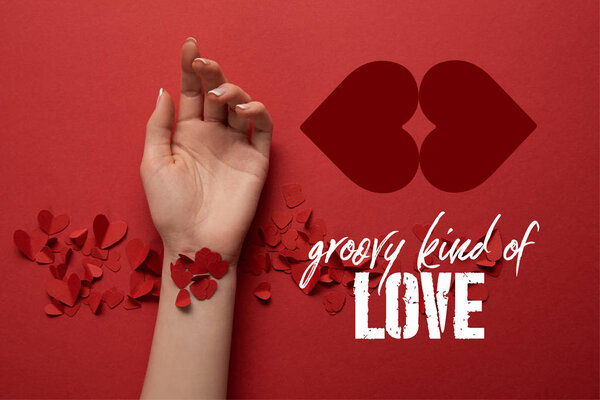 cropped view of female hand with paper cut decorative hearts on red background with "groovy kind of love" lettering 