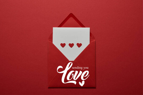 top view of "sending you love" lettering with hearts in envelope on red background