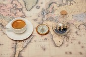 Selektivní fokus kávy šálek a talířek, kompas a hračka lodi v láhvi skla na mapě