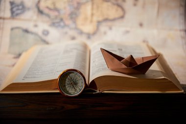 Selective focus of paper boat, book, map and compass on table clipart