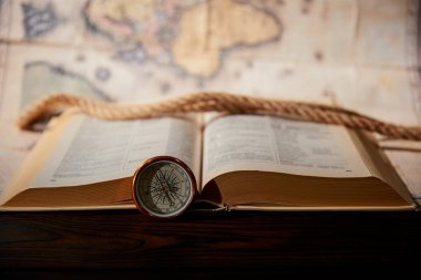Selective focus of rope, map, book and compass on wooden table clipart
