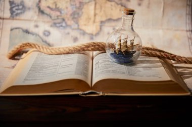 Selective focus of toy ship in glass bottle, book, map and rope on table clipart