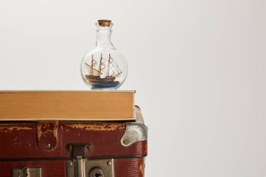 toy ship in glass bottle and book on brown suitcase with copy space  clipart