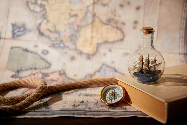 Selective focus of toy ship in glass bottle, book, map and rope on table
