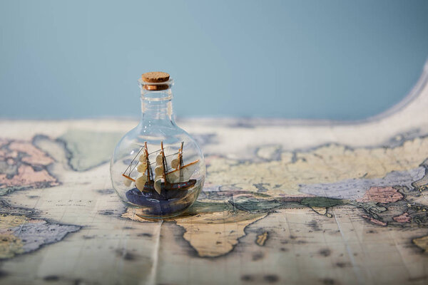 Selective focus of toy ship in glass bottle and map with copy space isolated on blue