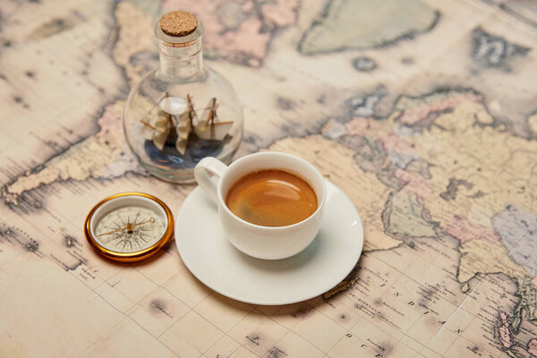 selective focus of coffee cup, compass and toy ship in glass bottle on map