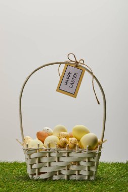 easter chicken and quail eggs in straw basket with flower and card with happy easter lettering on grass clipart