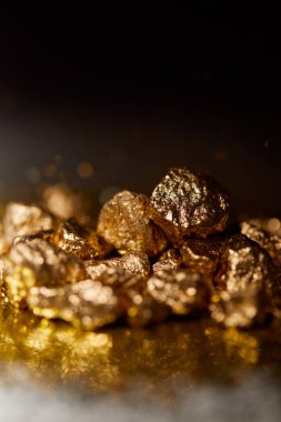 selective focus of golden stones on dark sparkling surface and black background clipart