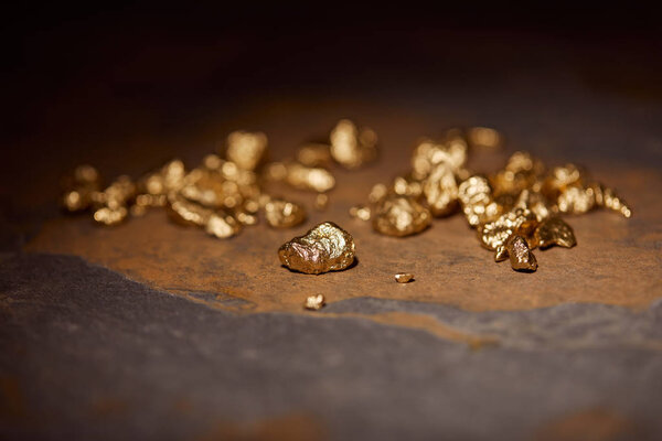 selective focus of golden stones on grey and brown marble surface with blurred dark background