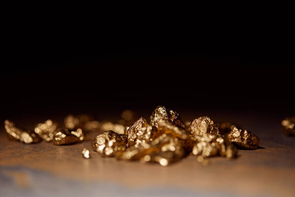 selective focus of golden stones on grey and brown marble surface with blurred black background