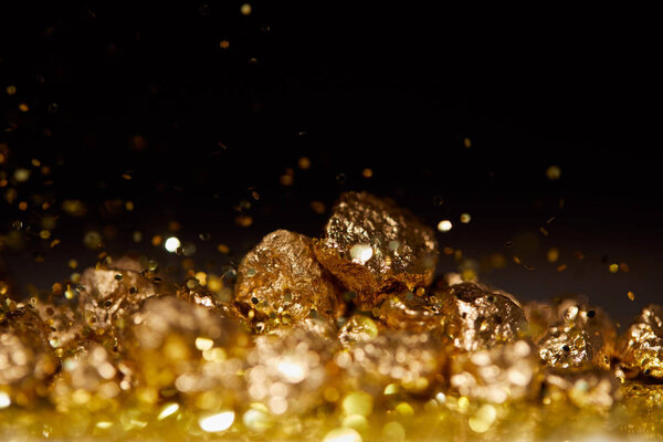selective focus of golden stones on sparkling surface and black background