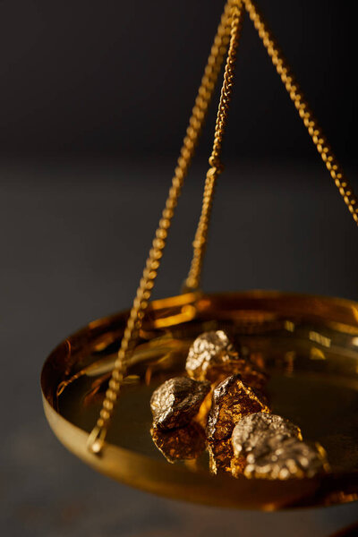 selective focus of golden stones on vintage scales on dark background