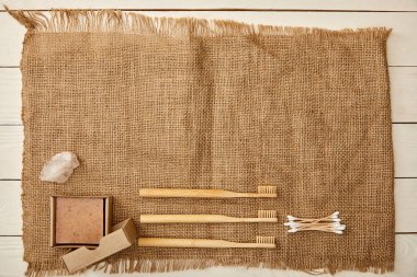 top view of different hygiene and care items arranged on sackcloth on white wooden surface, zero waste concept clipart