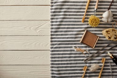 Beyaz ahşap yüzey, sıfır atık kavramı üzerinde çizgili havlu üzerinde düzenlenmiş farklı hijyen ve bakım öğeleri üstten görünüm 