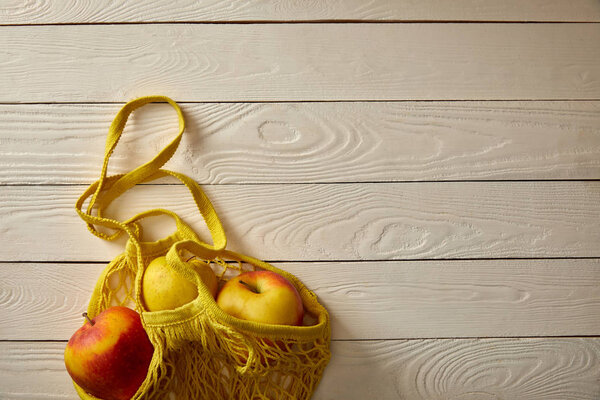 top view of string bag with rape apples on white wooden surface, zero waste concept