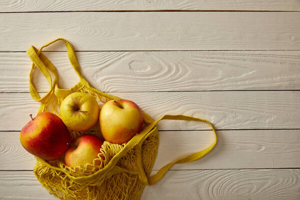 top view of string bag full of rape apples on white wooden surface, zero waste concept