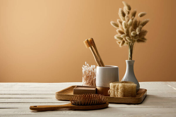 wooden tray with different hygiene and care items, vase of spikelets, and hair brush on white wooden surface, zero waste concept