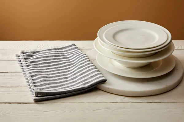 一叠白色的盘子和条纹的棉毛巾在白色木表面 — 图库照片
