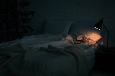 kitap ve boş yatak, bitki ve lamba gece siyah komodinin üzerinde gözlük