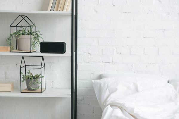 rack with plants, alarm clock and white bed 