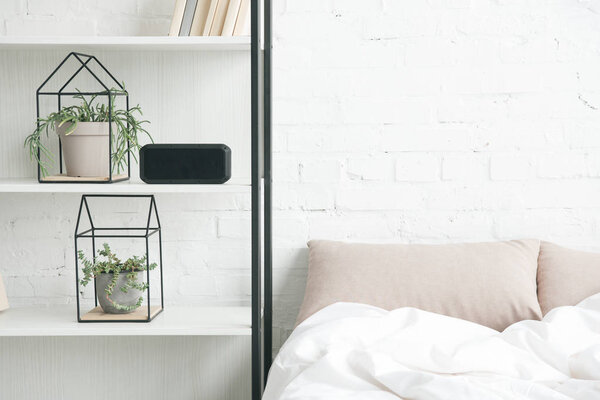 rack with plants, alarm clock and empty bed 