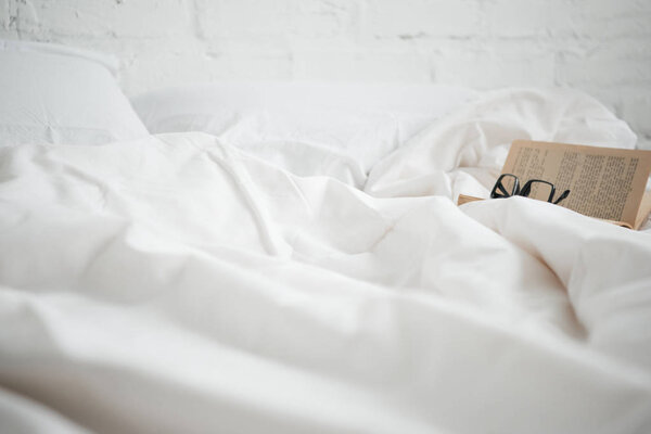 Selective focus of book with glasses on white bed 