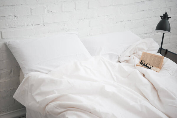 Очки и забронировать на кровать с белым одеялом и подушки, лампы
