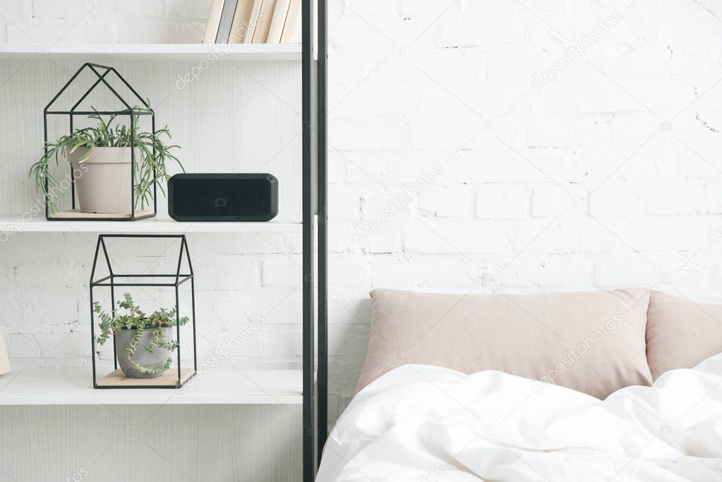 rack with plants, alarm clock and empty bed 