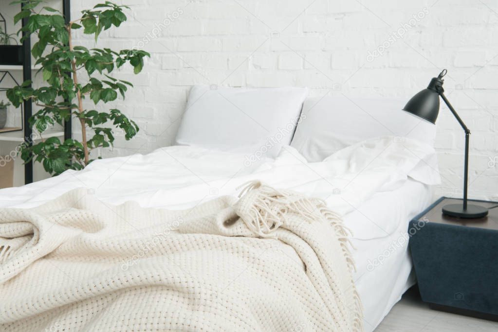 bed with white blanket and pillows, plant and lamp on black nightstand