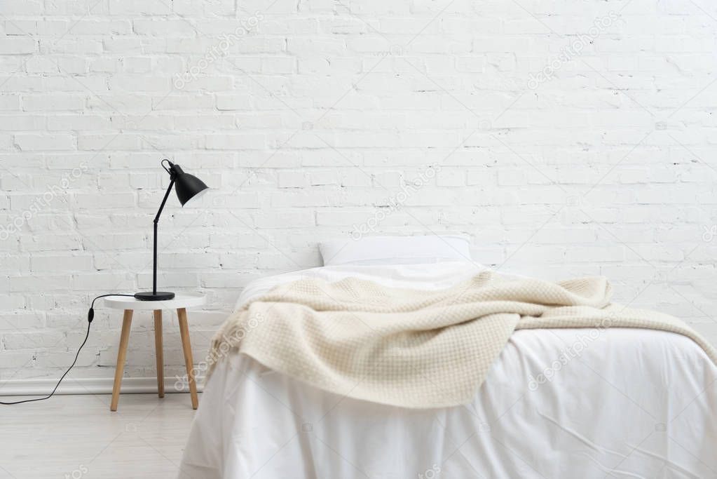 Interior of cozy bedroom with pillow on bed and lamp on stool