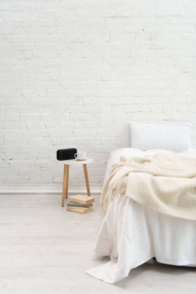 Interior of cozy bedroom with books, pillow on bed, alarm clock and coffee cup on stool