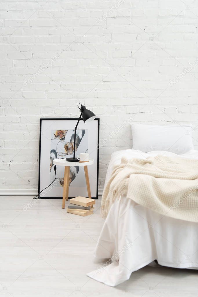 bedroom with books, picture, pillow on bed, lamp and coffee cup on stool