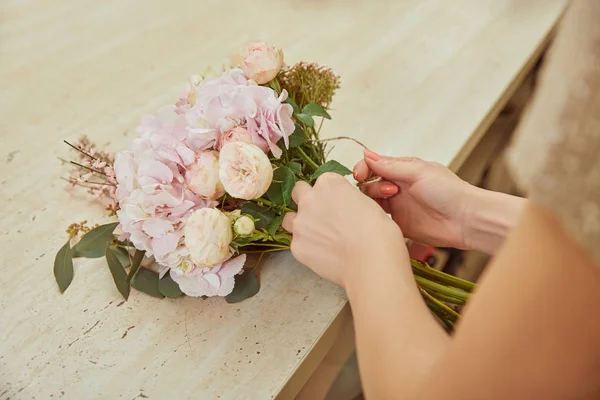 ベージュのバラとワークスペースでシャクヤクの花束を作る花屋の部分的なビュー — ストック写真